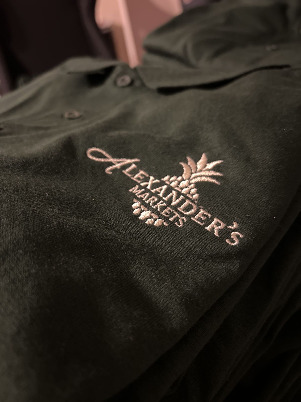 Black company polo with an embroidered Alexander's Markets logo