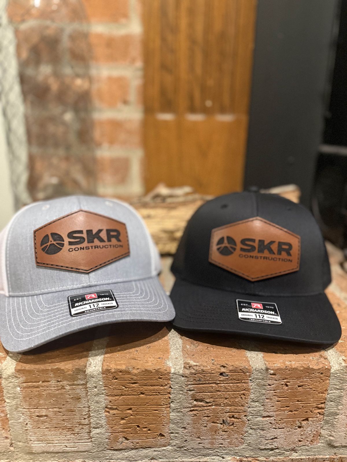 Gray and black trucker hats with SKR Construction leather patches